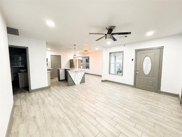 kitchen featuring a kitchen island with sink, hanging light fixtures, ceiling fan, light hardwood / wood-style flooring, and fridge