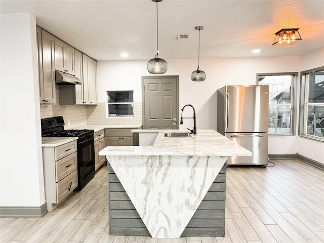 kitchen featuring an island with sink, black gas range oven, gray cabinets, stainless steel refrigerator, and sink