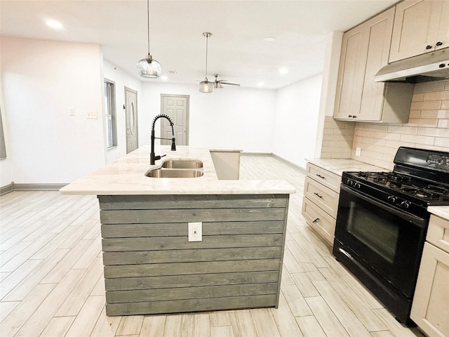 kitchen featuring black gas range, an island with sink, light stone countertops, sink, and decorative light fixtures