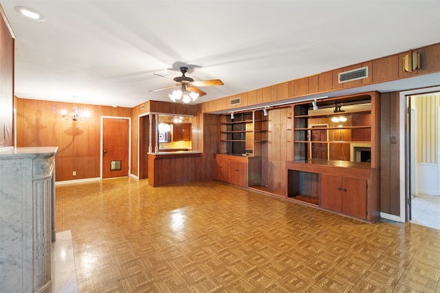 unfurnished living room featuring wood walls, light parquet floors, and ceiling fan with notable chandelier