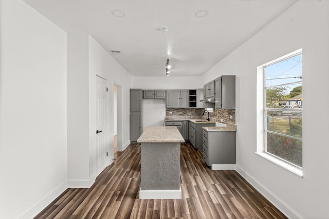 kitchen featuring dark wood-type flooring, a kitchen island, gray cabinetry, and sink