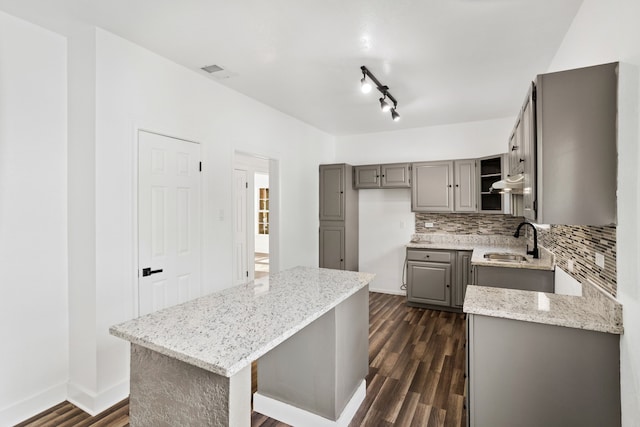 kitchen with a center island, sink, gray cabinets, dark hardwood / wood-style flooring, and light stone counters