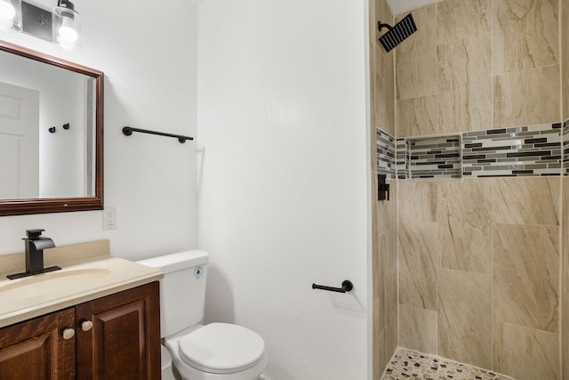 bathroom featuring a tile shower, vanity, and toilet