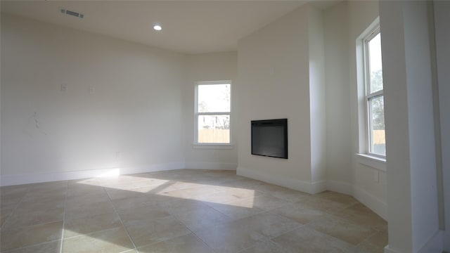 unfurnished living room with light tile patterned flooring, a glass covered fireplace, and baseboards