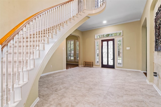 entryway with arched walkways, crown molding, a towering ceiling, and baseboards