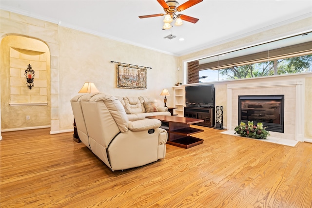 living room with ceiling fan, light hardwood / wood-style floors, crown molding, and a tile fireplace