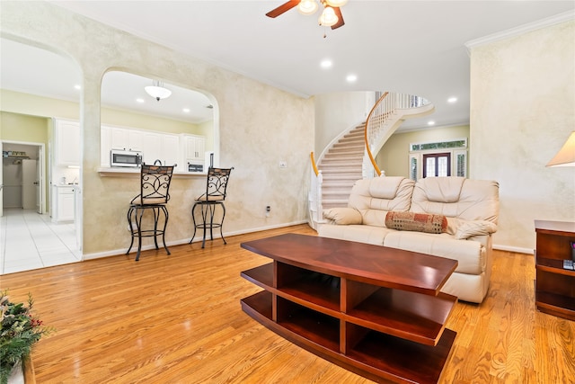 living room with ceiling fan, light wood-type flooring, and ornamental molding