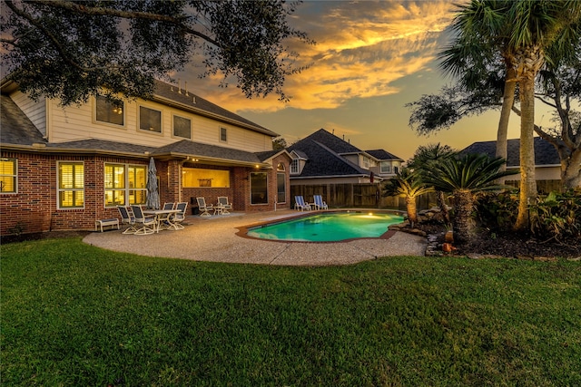 pool at dusk with a patio area and a lawn