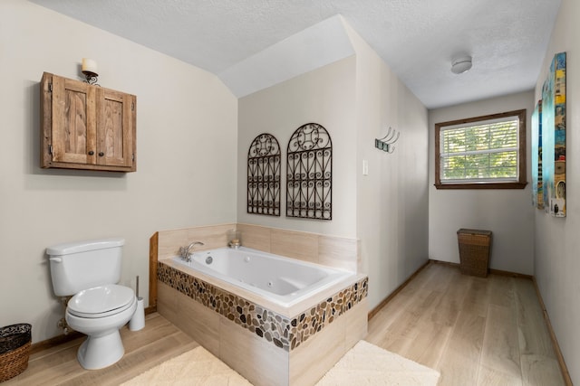 bathroom featuring hardwood / wood-style floors, a relaxing tiled tub, toilet, and a textured ceiling