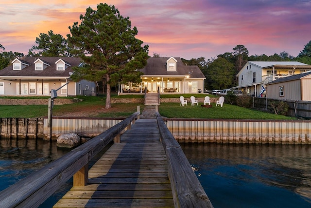 view of dock featuring a lawn, a water view, and fence