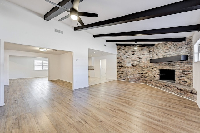 unfurnished living room with beamed ceiling, light wood-type flooring, ceiling fan, and brick wall