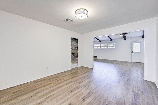 spare room with beam ceiling, light hardwood / wood-style flooring, and a textured ceiling