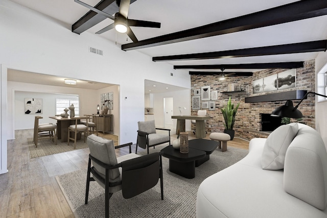 living room with ceiling fan, light wood-type flooring, a towering ceiling, beam ceiling, and brick wall