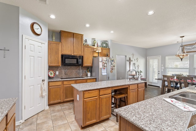 kitchen featuring light tile patterned floors, a center island, decorative light fixtures, and black appliances