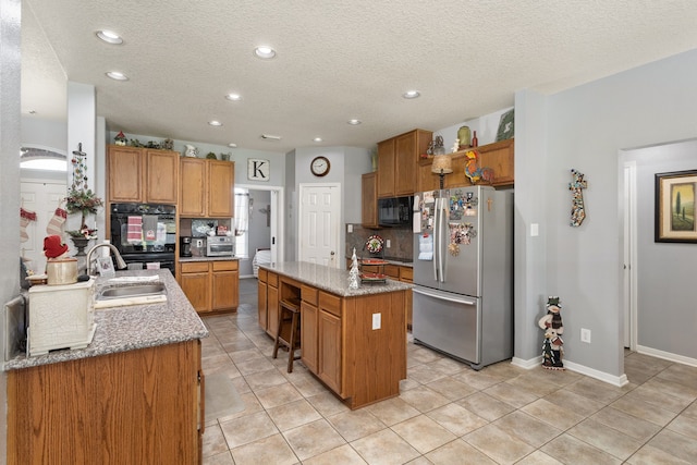 kitchen featuring backsplash, black appliances, sink, an island with sink, and light tile patterned flooring