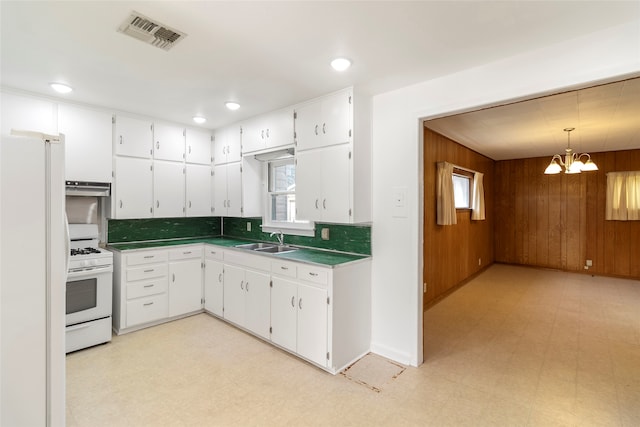 kitchen featuring white appliances, white cabinetry, sink, hanging light fixtures, and wood walls