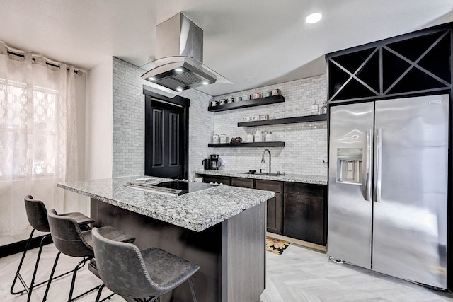 kitchen with island exhaust hood, stainless steel fridge, black stovetop, and light stone countertops