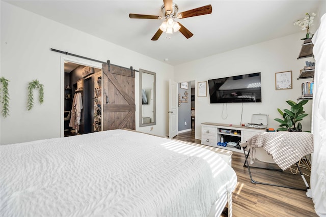 bedroom with hardwood / wood-style flooring, ceiling fan, and a barn door