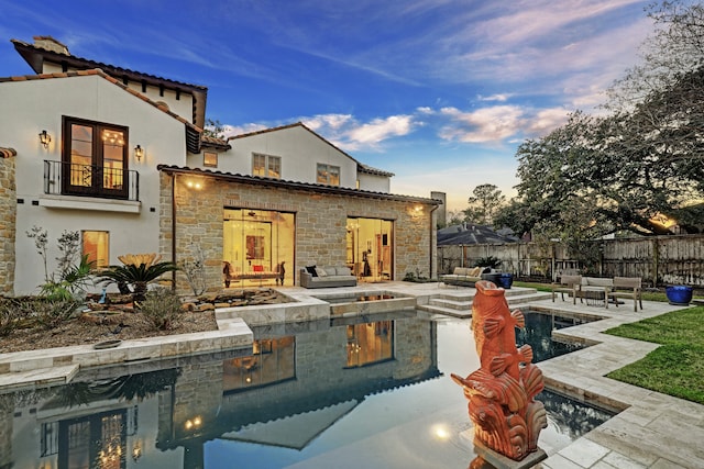 back house at dusk with a fenced in pool, a patio area, a balcony, and an outdoor hangout area