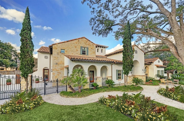 mediterranean / spanish-style home with a fenced front yard, stone siding, stucco siding, and a tile roof