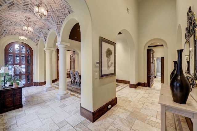 entryway with stone tile flooring, arched walkways, brick ceiling, baseboards, and ornate columns