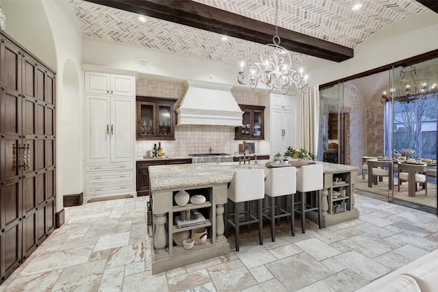 kitchen featuring custom exhaust hood, brick ceiling, and a center island with sink