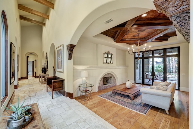 living room featuring coffered ceiling, light hardwood / wood-style floors, beam ceiling, and a notable chandelier