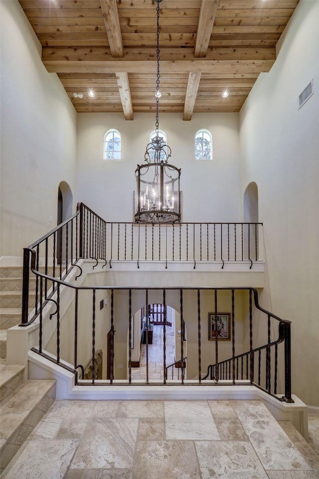 stairway featuring a notable chandelier, beam ceiling, plenty of natural light, and wooden ceiling