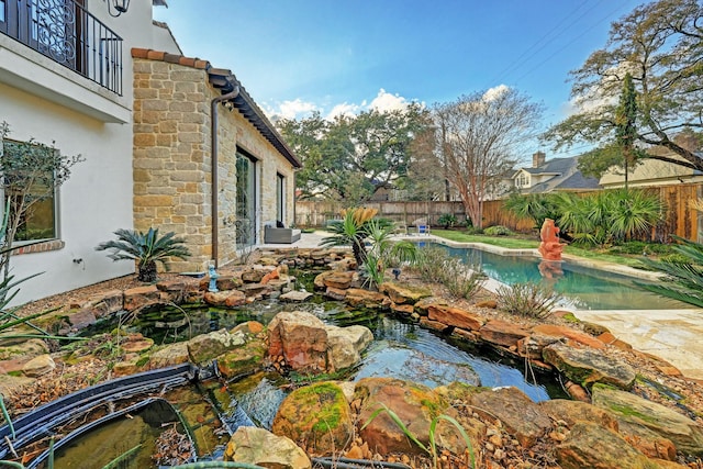 view of pool featuring a fenced in pool, a small pond, a fenced backyard, and a patio area