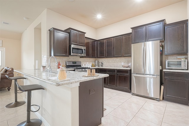 kitchen featuring light stone countertops, appliances with stainless steel finishes, tasteful backsplash, dark brown cabinets, and kitchen peninsula