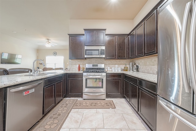 kitchen with decorative backsplash, appliances with stainless steel finishes, light stone counters, ceiling fan, and sink