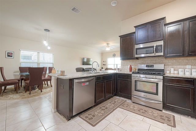 kitchen featuring kitchen peninsula, appliances with stainless steel finishes, decorative backsplash, sink, and decorative light fixtures