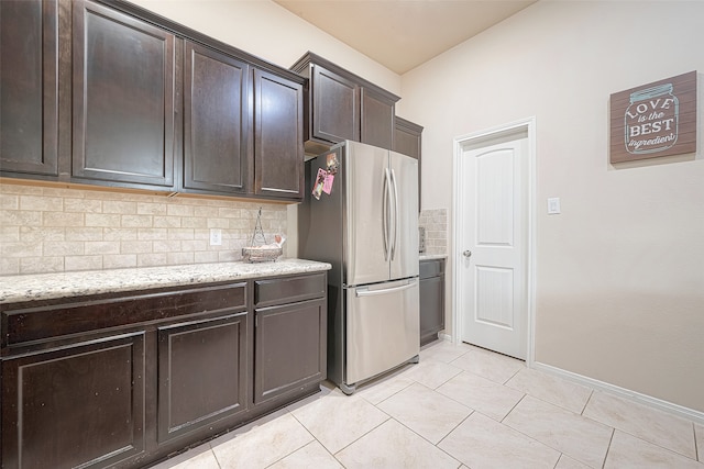 kitchen featuring stainless steel fridge, tasteful backsplash, light tile patterned flooring, light stone counters, and dark brown cabinetry