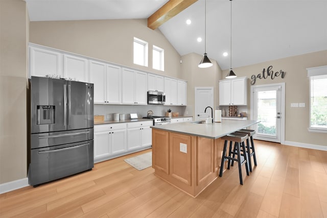 kitchen with appliances with stainless steel finishes, a center island with sink, light hardwood / wood-style flooring, beamed ceiling, and white cabinets