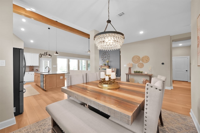 dining space featuring beamed ceiling, light wood-type flooring, an inviting chandelier, and sink