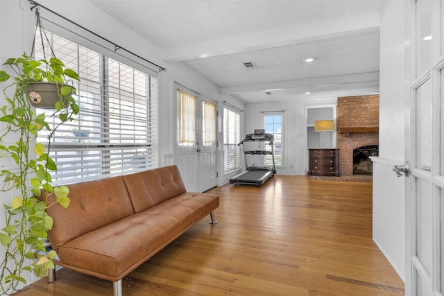 living room with a fireplace, beam ceiling, and wood-type flooring