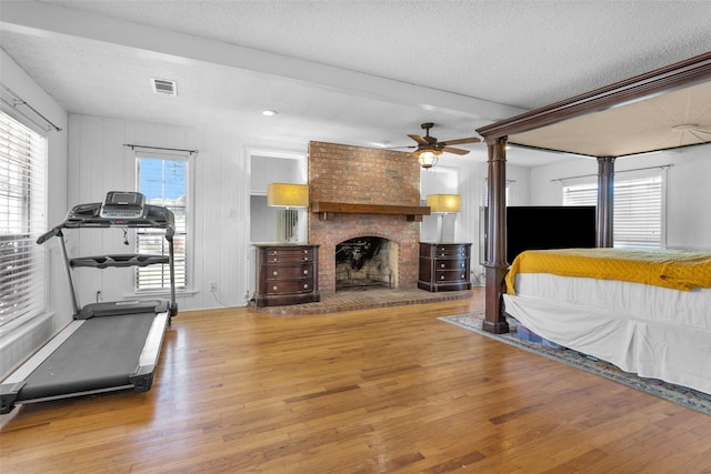 bedroom with hardwood / wood-style flooring, ceiling fan, a fireplace, and a textured ceiling