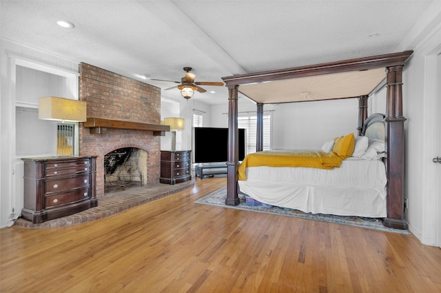 bedroom featuring ceiling fan, light hardwood / wood-style floors, a textured ceiling, and a fireplace