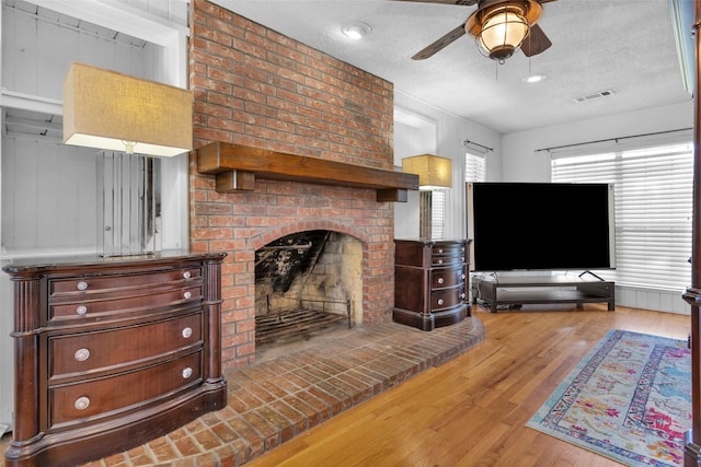 living room featuring a fireplace, hardwood / wood-style floors, a textured ceiling, and ceiling fan