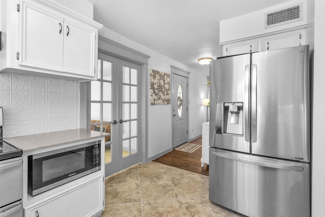 kitchen with white cabinets, decorative backsplash, appliances with stainless steel finishes, and french doors