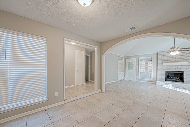 unfurnished living room with light tile patterned floors, a textured ceiling, a brick fireplace, and ceiling fan