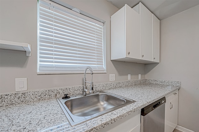 kitchen with white cabinets, light stone counters, stainless steel dishwasher, and sink