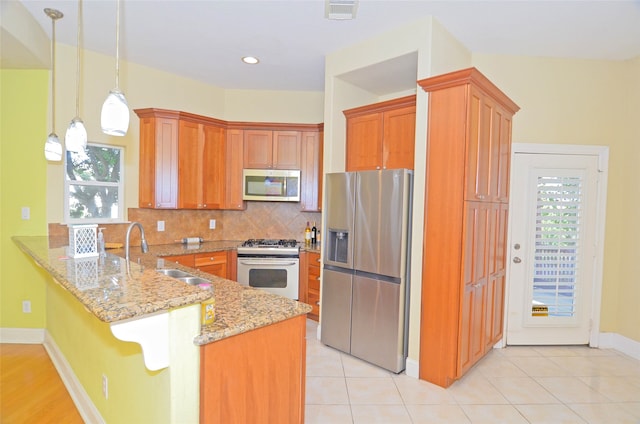 kitchen with sink, decorative light fixtures, kitchen peninsula, stainless steel appliances, and backsplash