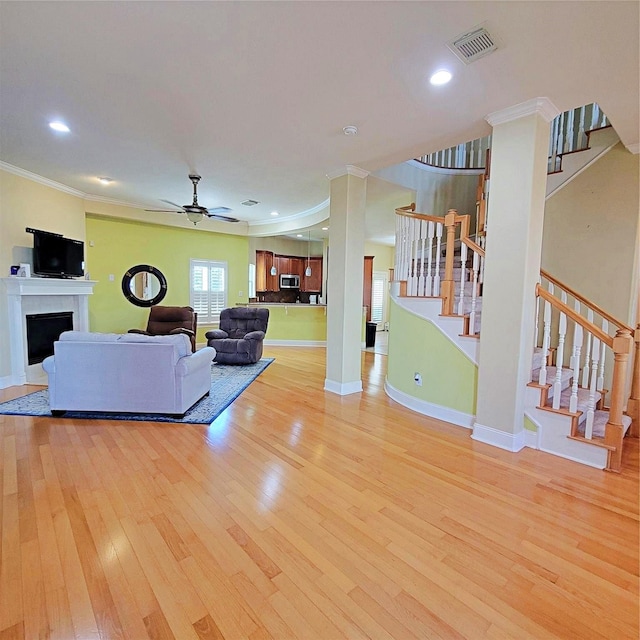 living room with crown molding, ceiling fan, a tile fireplace, and light wood-type flooring