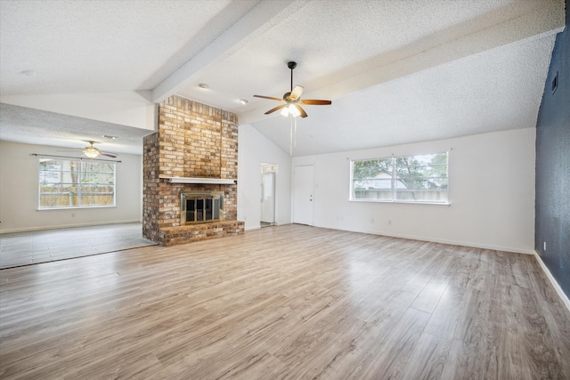 unfurnished living room featuring ceiling fan, a brick fireplace, vaulted ceiling with beams, hardwood / wood-style floors, and a textured ceiling