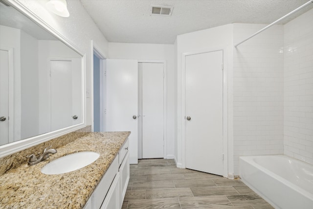 bathroom featuring hardwood / wood-style floors, vanity, a textured ceiling, and tiled shower / bath