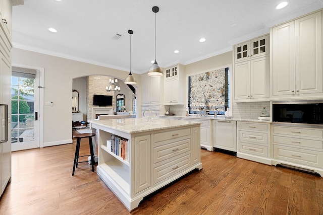 kitchen with decorative backsplash, light stone counters, crown molding, hardwood / wood-style floors, and a center island