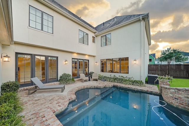 back house at dusk with a fenced in pool and a patio area