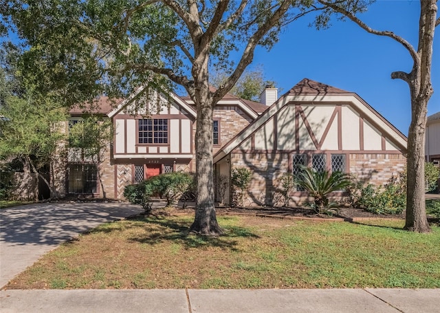 tudor-style house with brick siding, concrete driveway, a chimney, and a front lawn