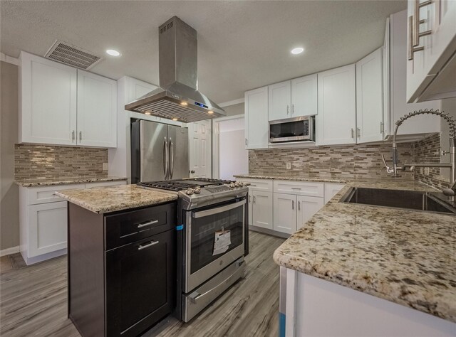 kitchen with appliances with stainless steel finishes, light wood-type flooring, wall chimney exhaust hood, sink, and white cabinets